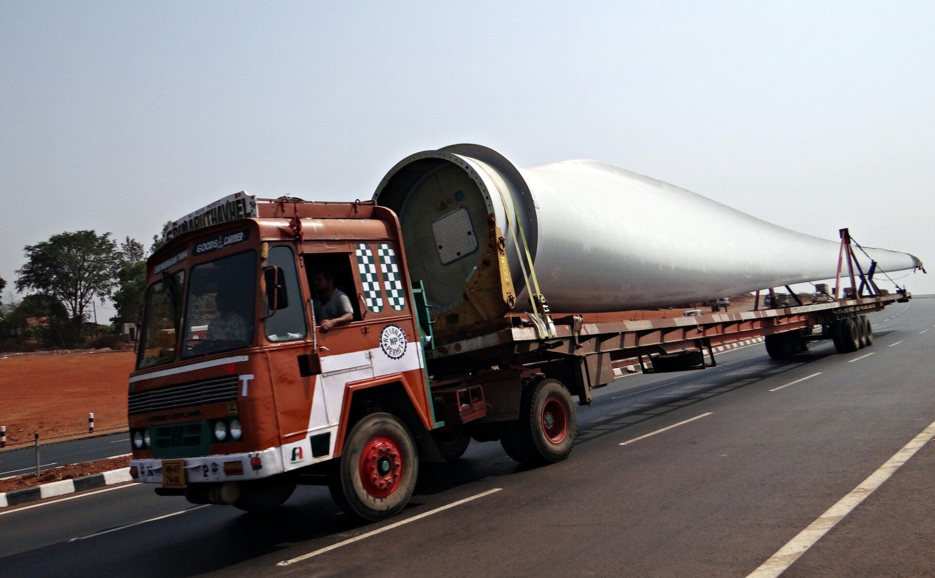 A truck is driving down a highway carrying a large cylinder