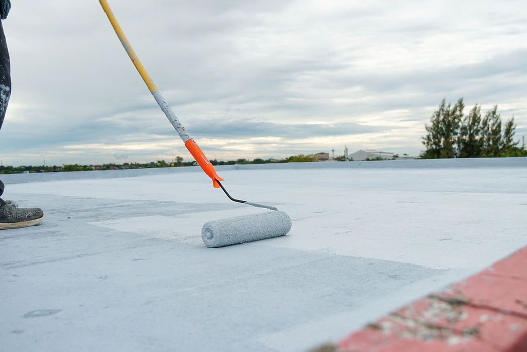 A person is painting a roof with a roller.