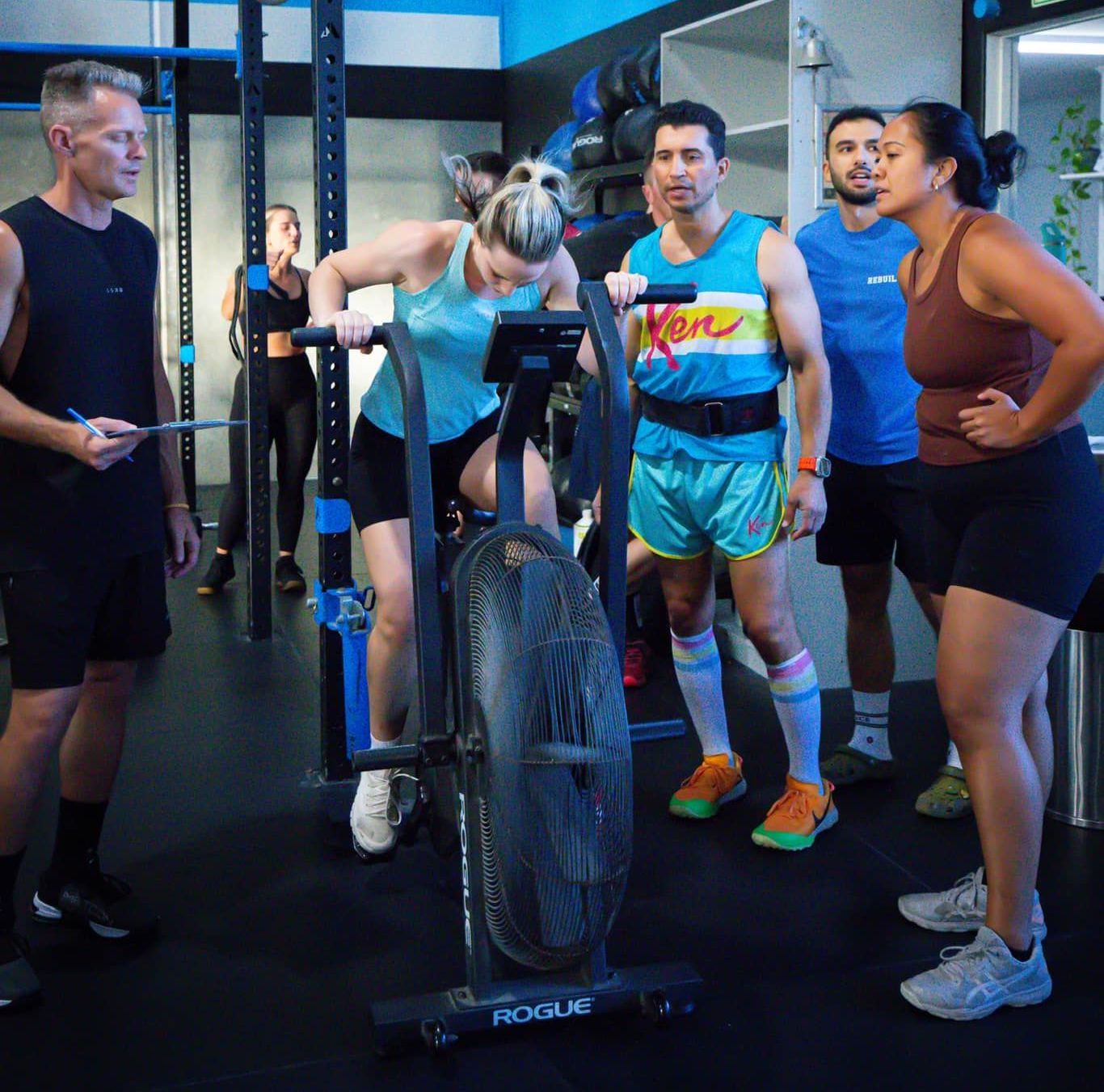 A group of people are standing around a rogue exercise bike