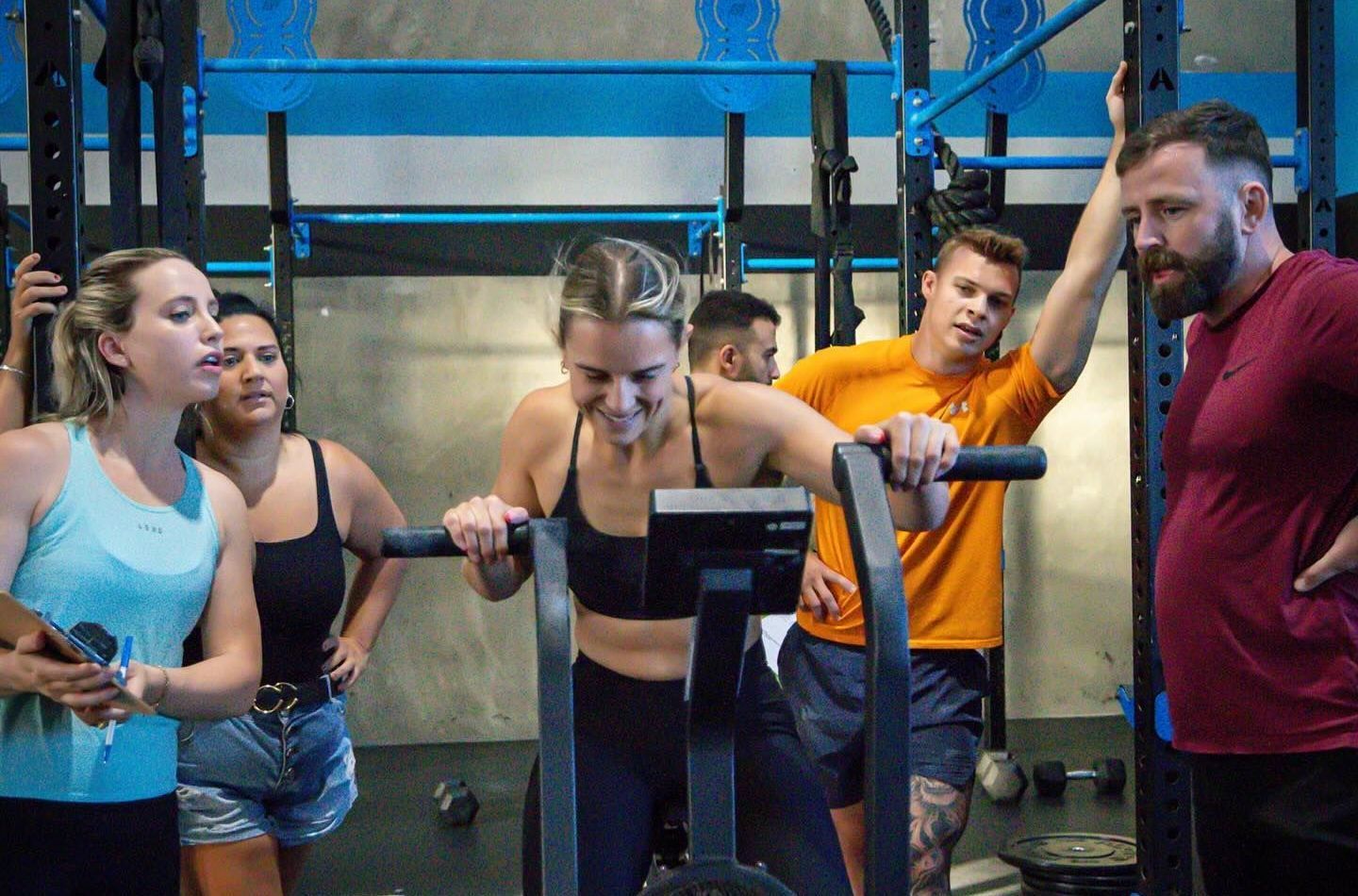 A group of people are standing around a woman riding an exercise bike in a gym.