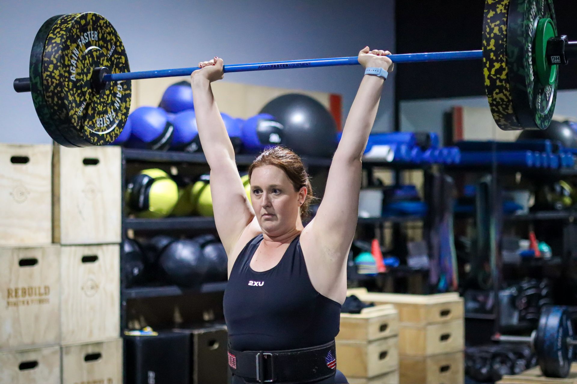 A woman is lifting a barbell over her head in a gym.