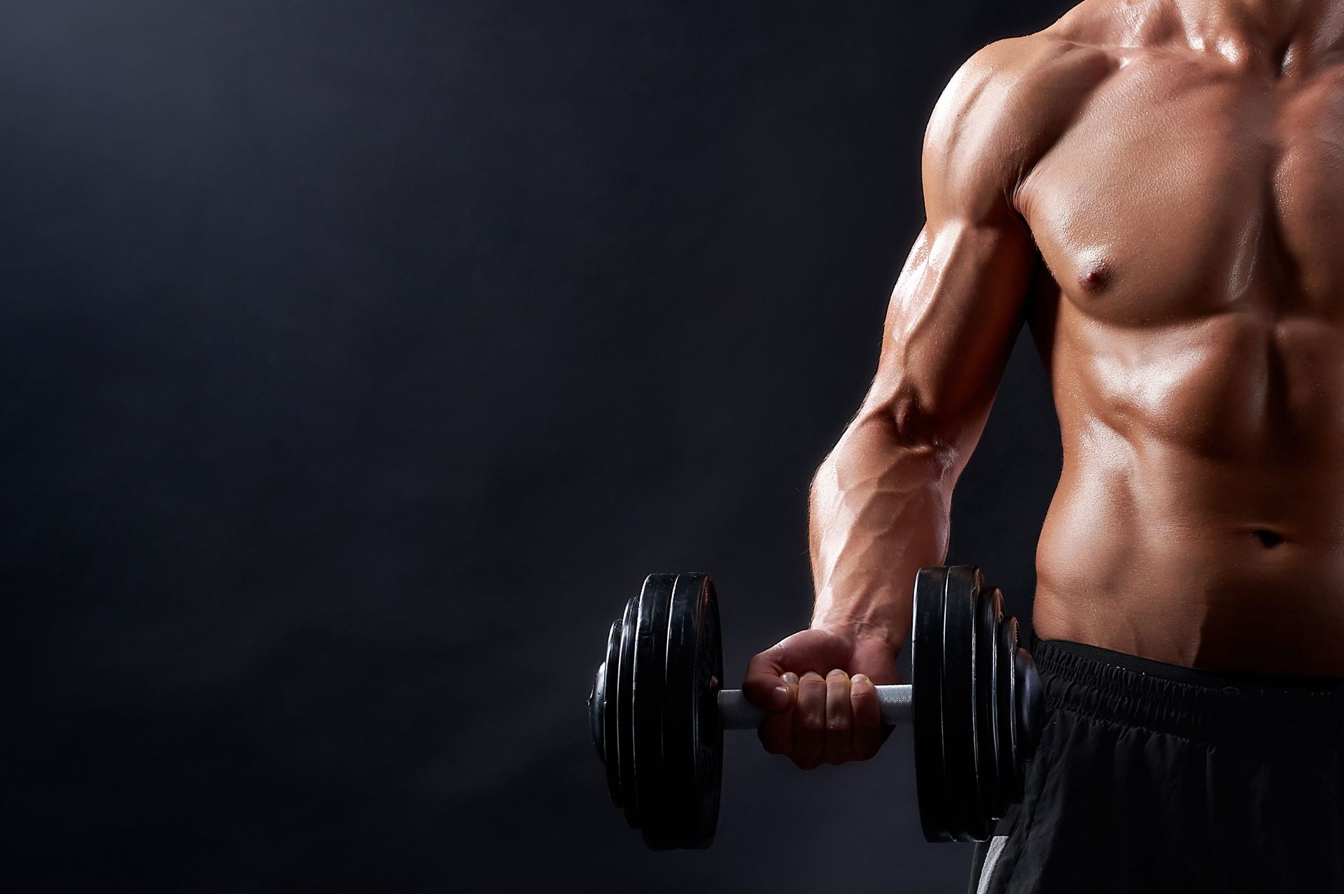 A shirtless man is holding a dumbbell in his hand.