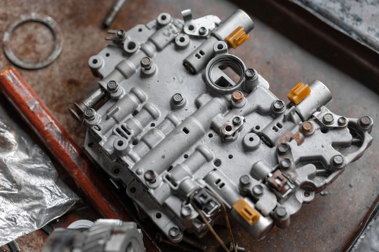 Corpo valvole motore o trasmissione in metallo argentato con tappi arancioni su un banco da lavoro