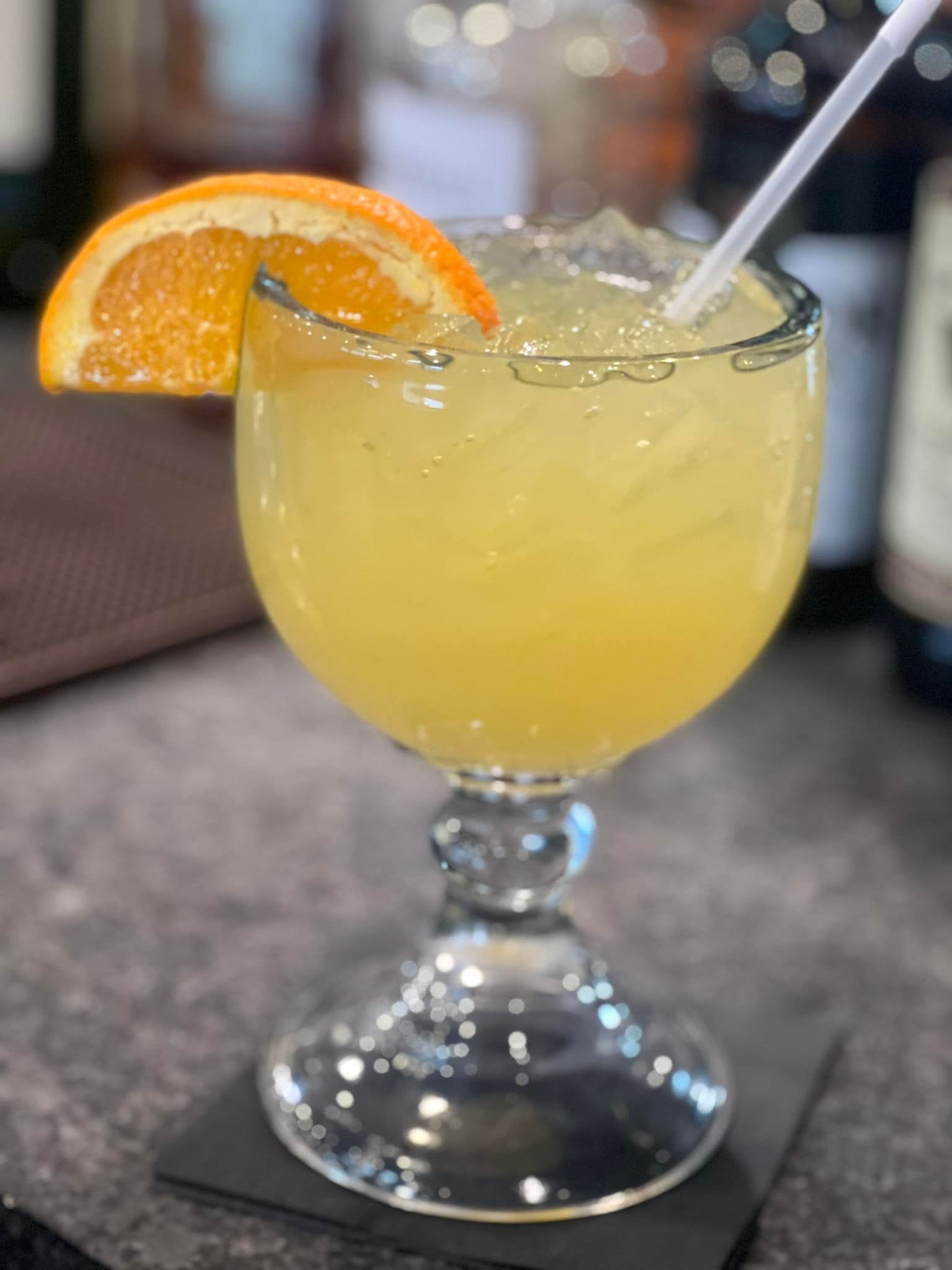 A close up of a margarita with an orange slice on a table.