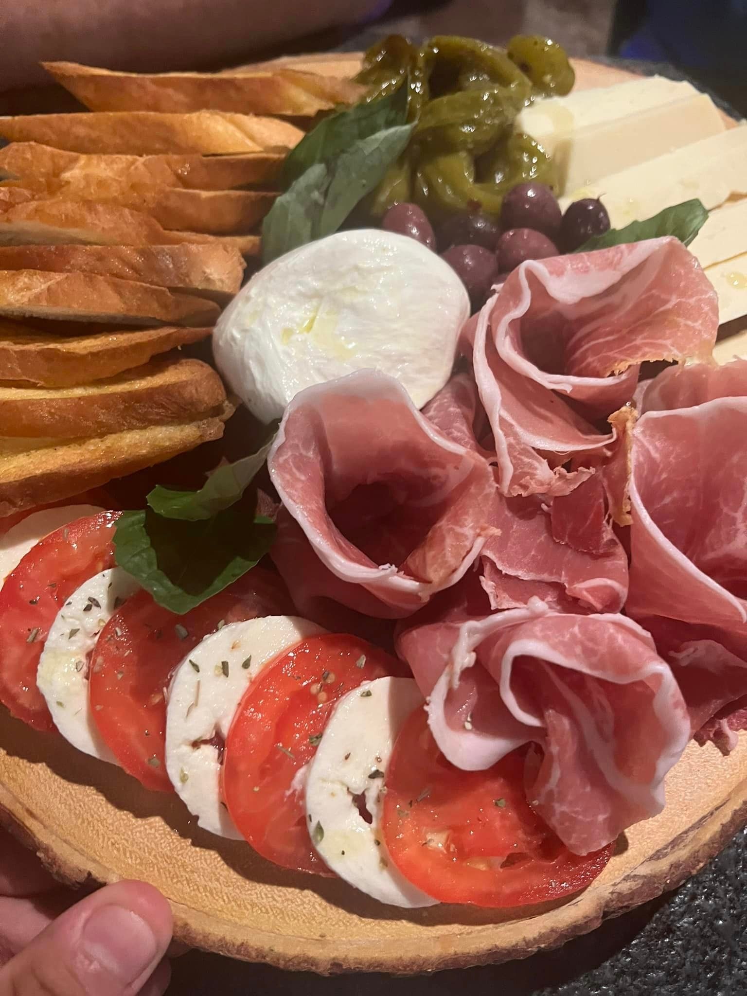 A person is holding a plate of food with meat , cheese , tomatoes and olives.