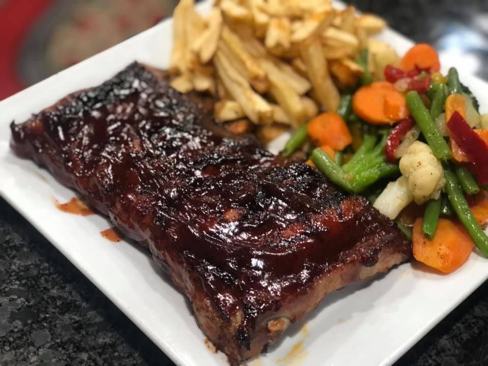 A white plate topped with ribs , french fries and vegetables.