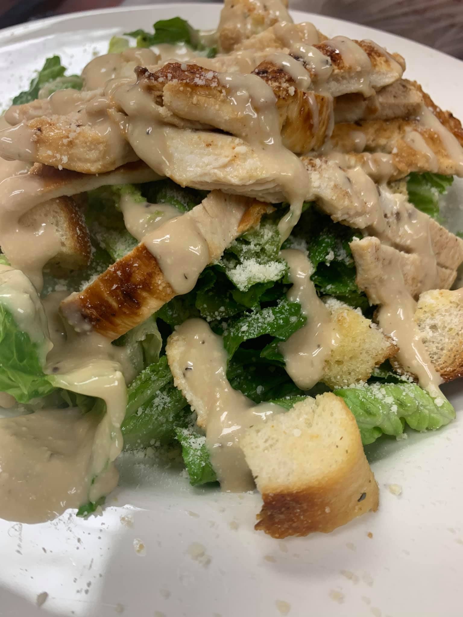 A close up of a caesar salad with chicken and lettuce on a plate.