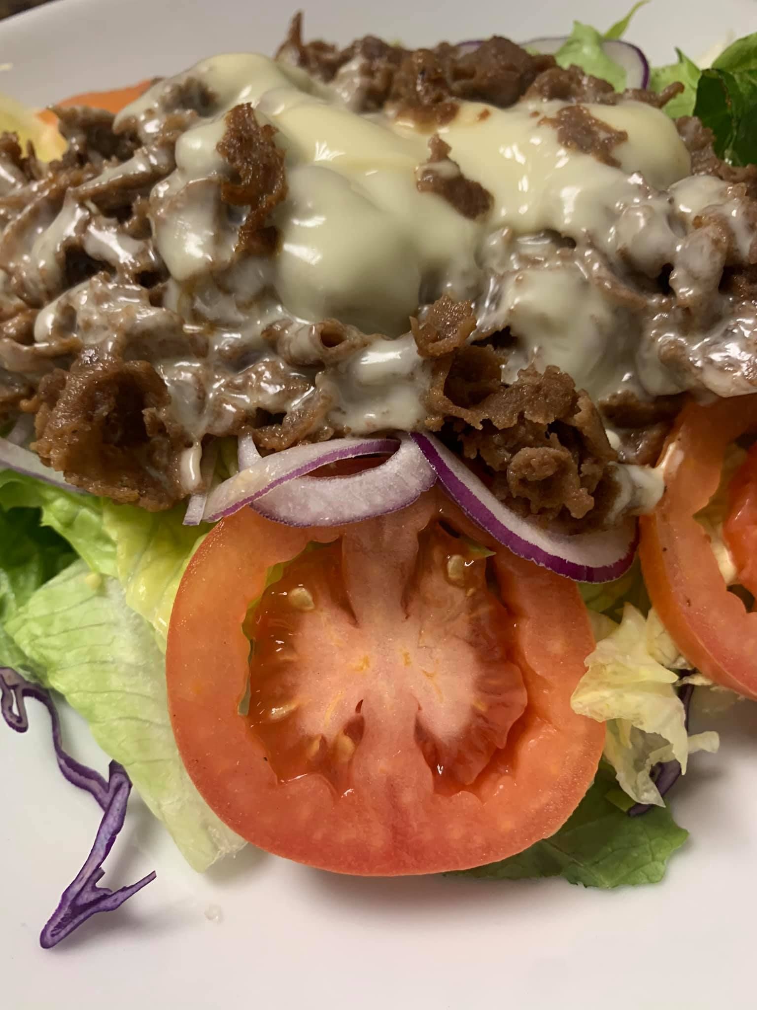 A close up of a salad with tomatoes , lettuce , onions and cheese on a plate.