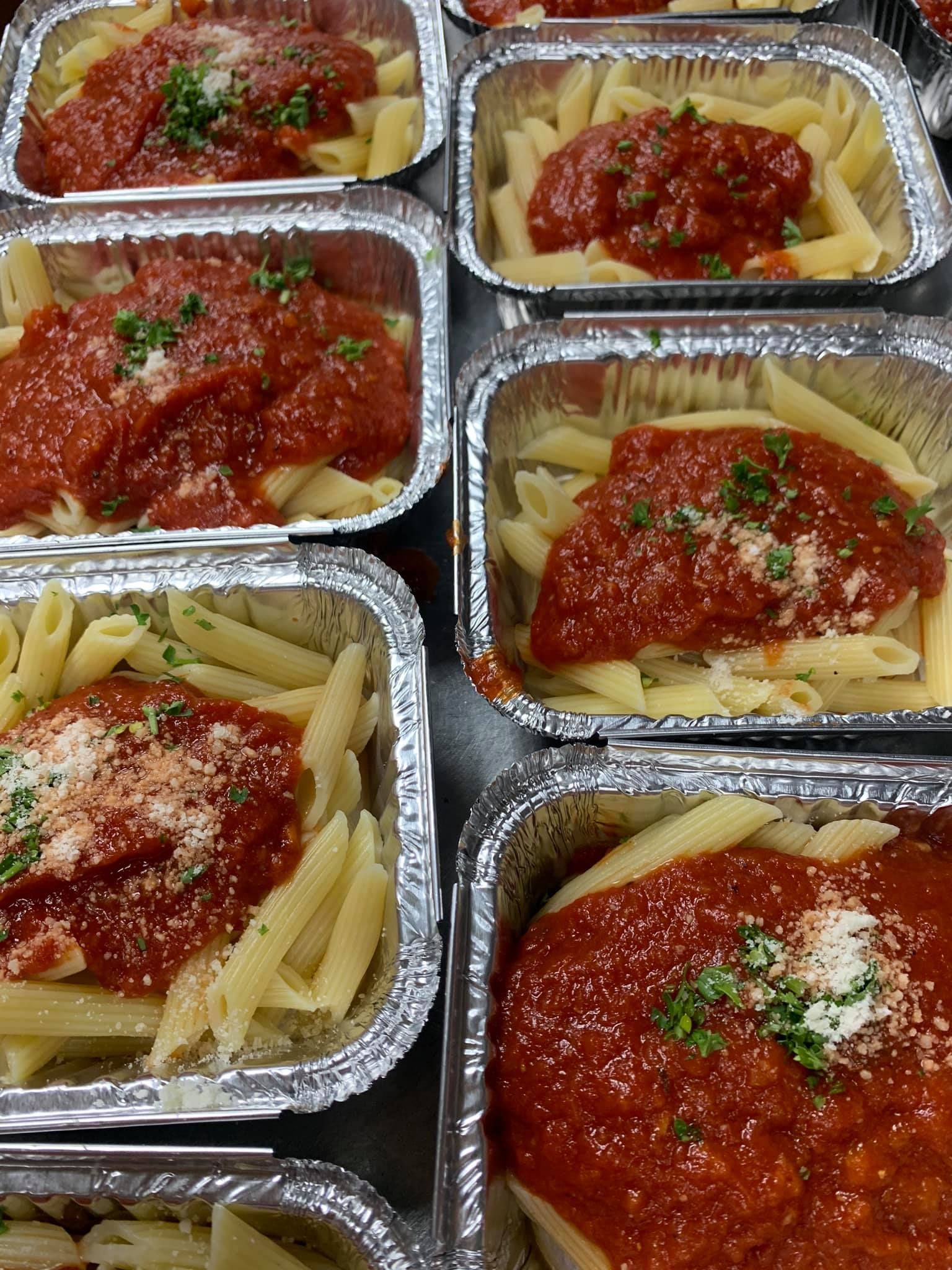 A bunch of aluminum foil containers filled with pasta and sauce.