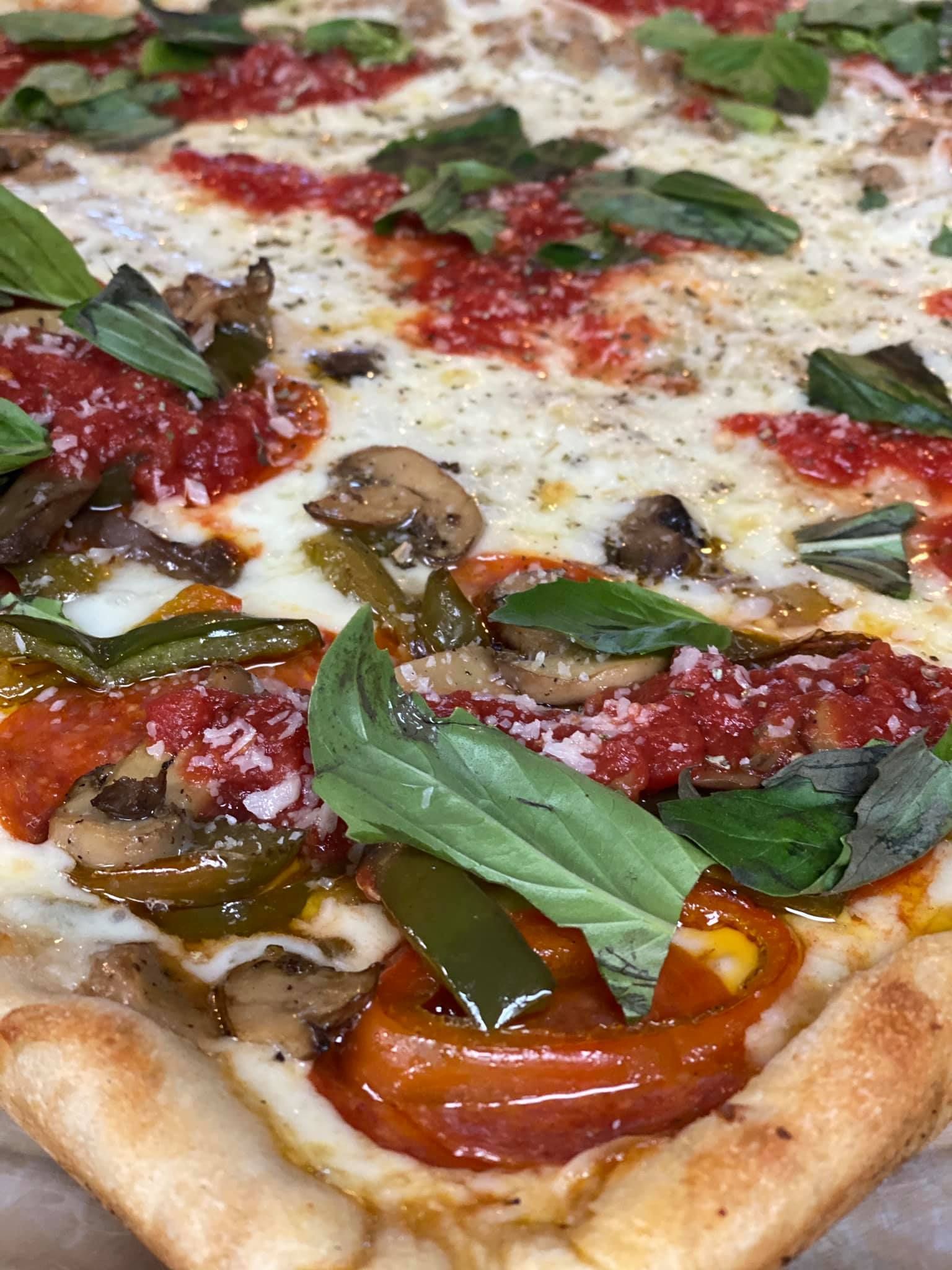 A pizza with tomato sauce , mushrooms , peppers and basil on it.