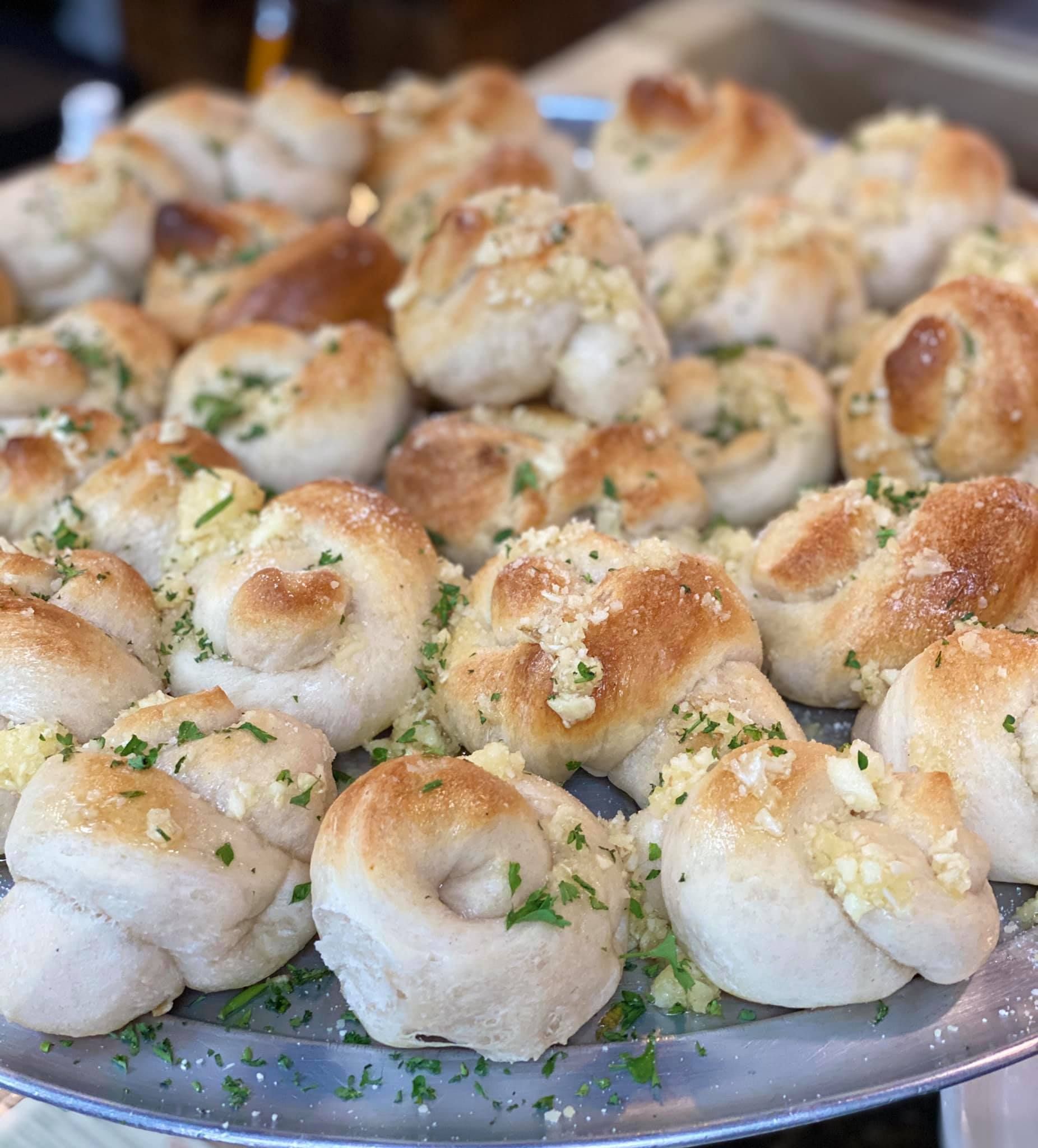 A close up of a plate of garlic knots on a table.