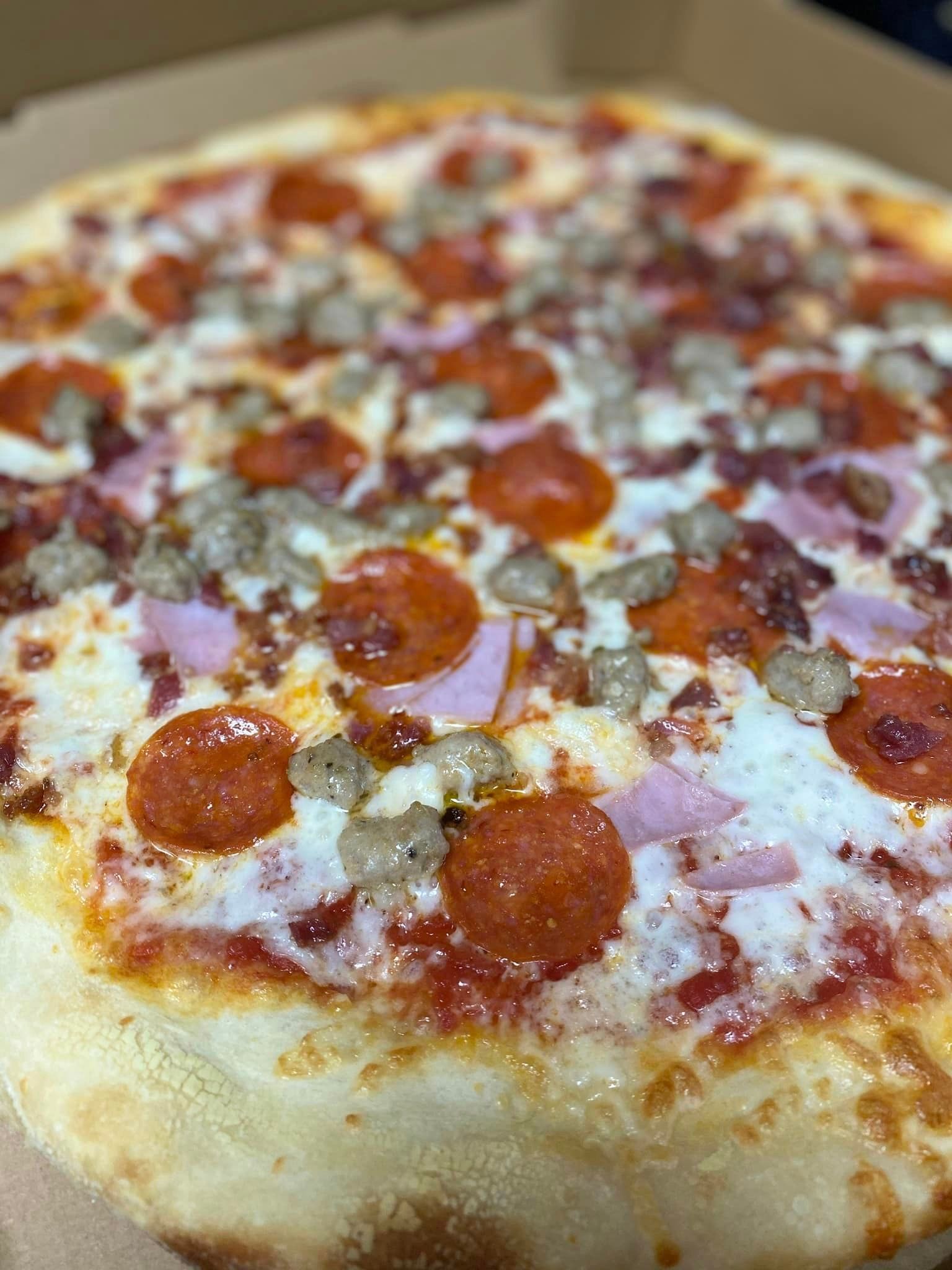 A pizza with pepperoni , ham and sausage on it is in a box.