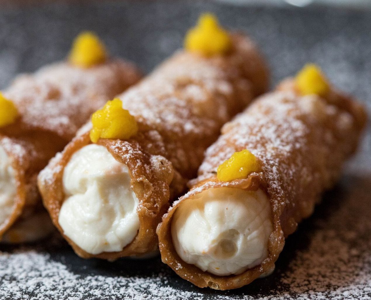 A close up of three cannoli with powdered sugar and yellow frosting on a table.