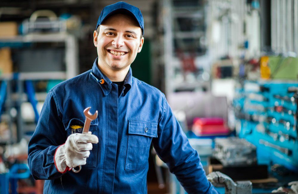 Mechanic in Blue Uniform, Holding a Wrench, Smiles in a Workshop — Auto Electrical Service in Mackay, QLD
