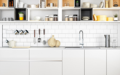Modern white kitchen with open shelves, subway tile backsplash, hanging mugs, and countertop decor.