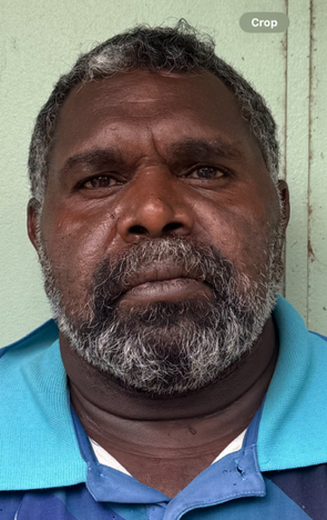 Man with dark skin and graying beard, wearing a blue shirt, looking directly at the camera.