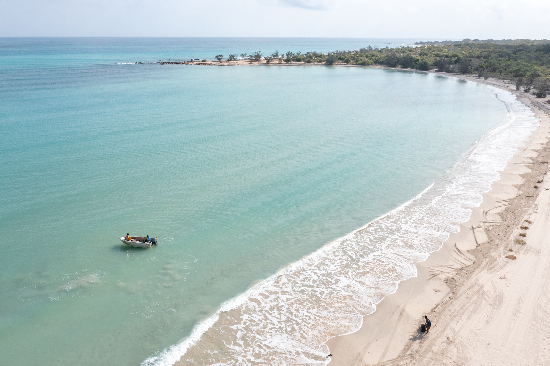 Blue ocean and sandy beach with a small boat and one person sitting on the shore.