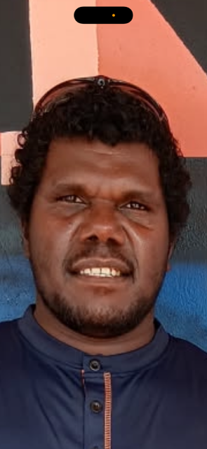 Man with dark skin, curly dark hair, and a navy blue shirt smiles. Sunglasses on top of head.