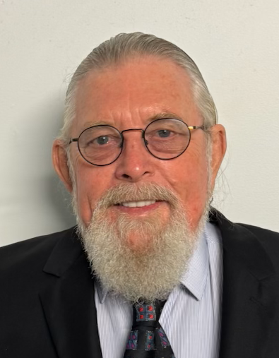 A man with a white beard and glasses, wearing a suit, smiles at the camera.