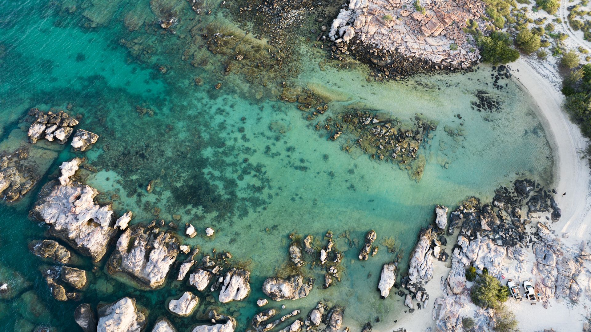 Aerial view of turquoise water, rocky shore, and small sandy beach.