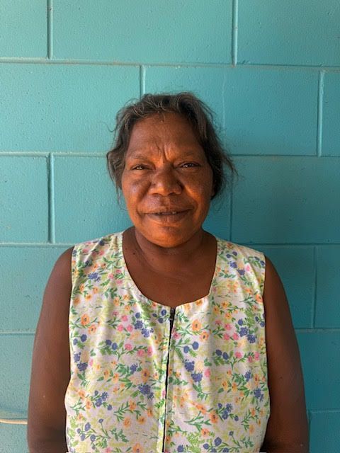 Woman in floral top against a turquoise block wall smiles at the camera.
