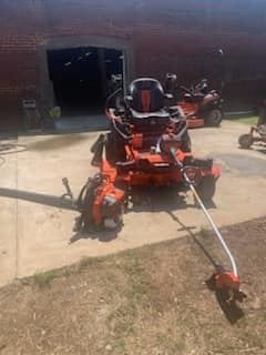 A lawn mower with a trimmer attached to it is parked in a driveway.