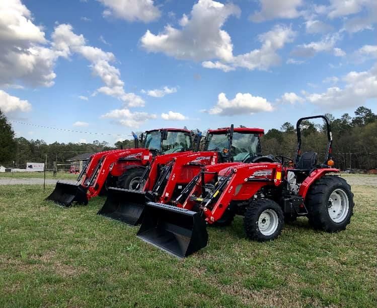 Three red tractors are parked in a grassy field.