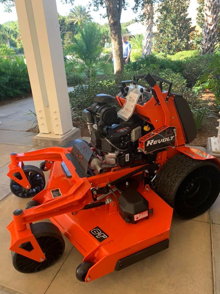 An orange lawn mower is parked on a sidewalk.