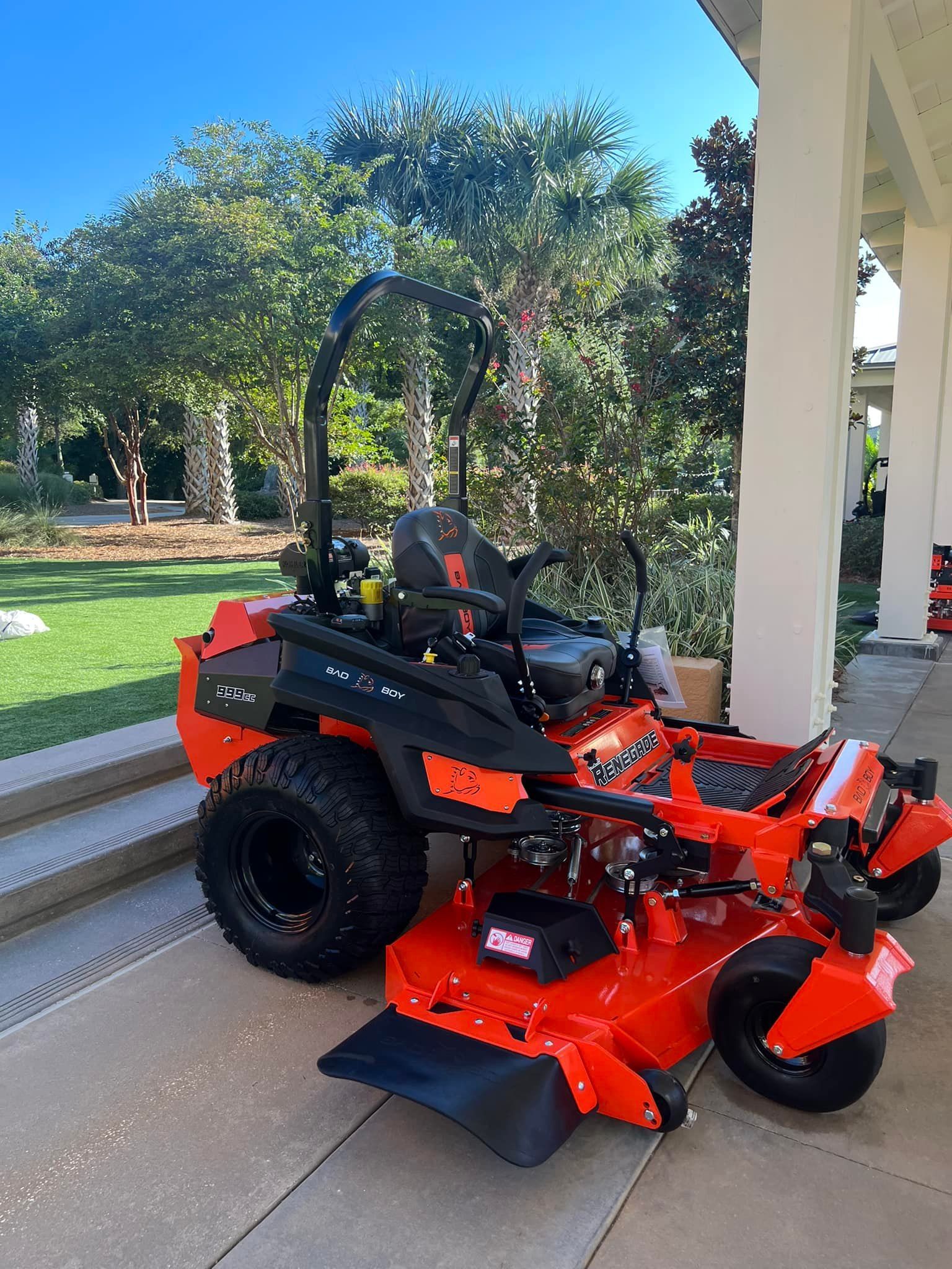 A red and black lawn mower is parked in front of a house.