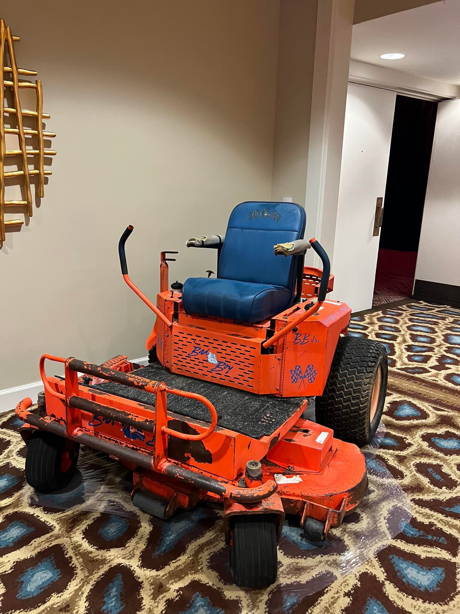 An orange lawn mower is sitting on a carpet in a room.