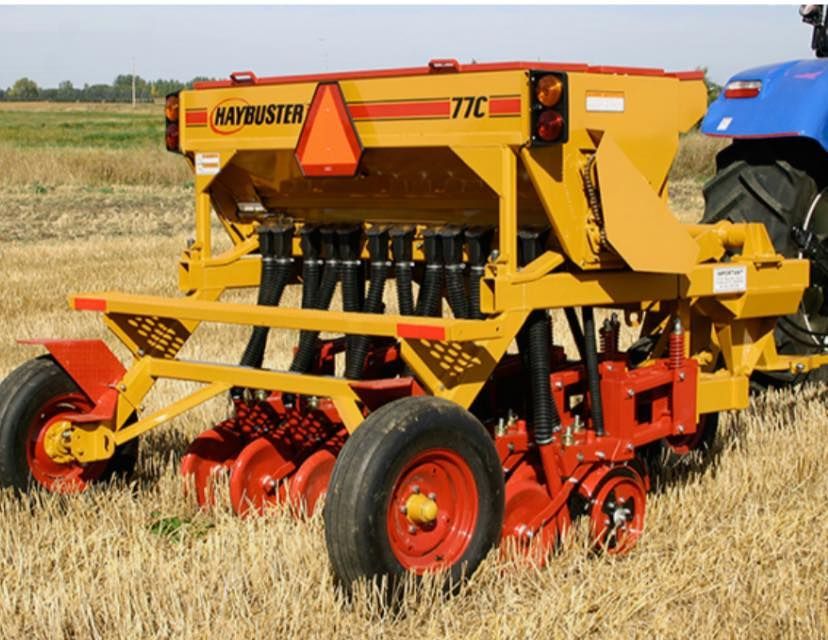 A yellow and red hay buster tractor is parked in a field
