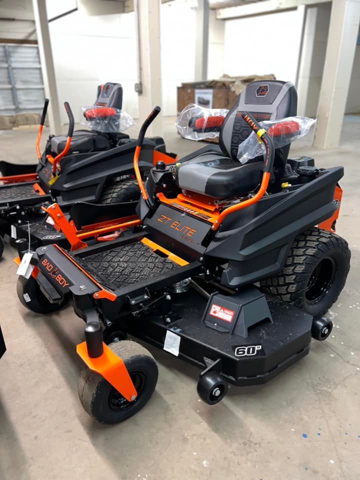 A row of black and orange lawn mowers are sitting in a warehouse.