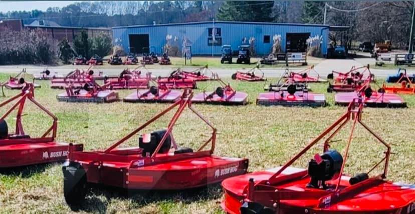 A bunch of red tractors are parked in a field in front of a building.