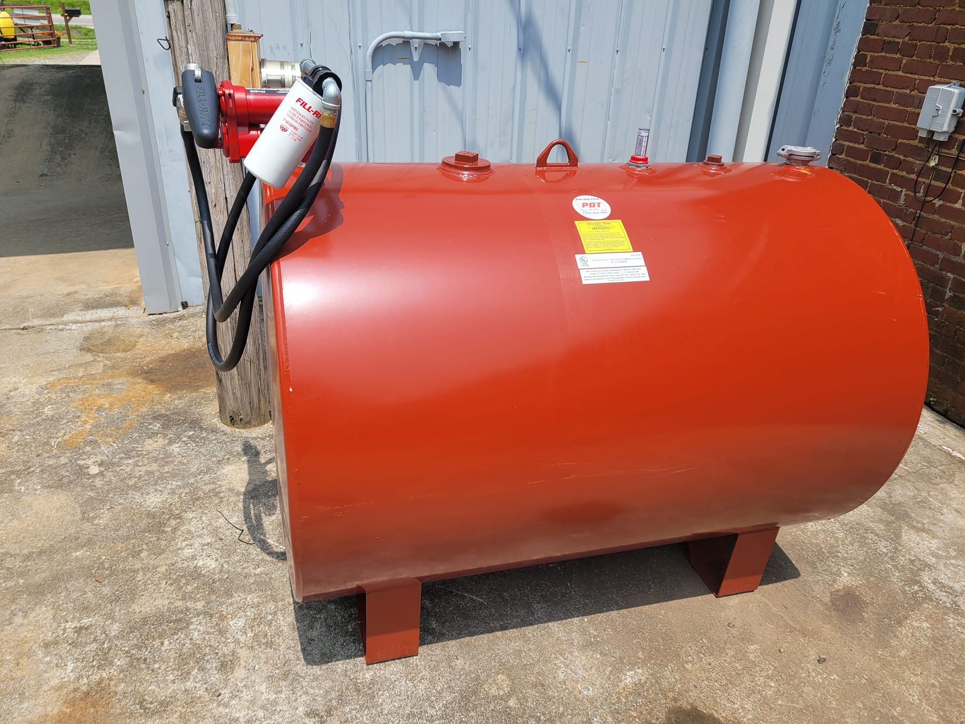 A red fuel tank is sitting in front of a brick building.