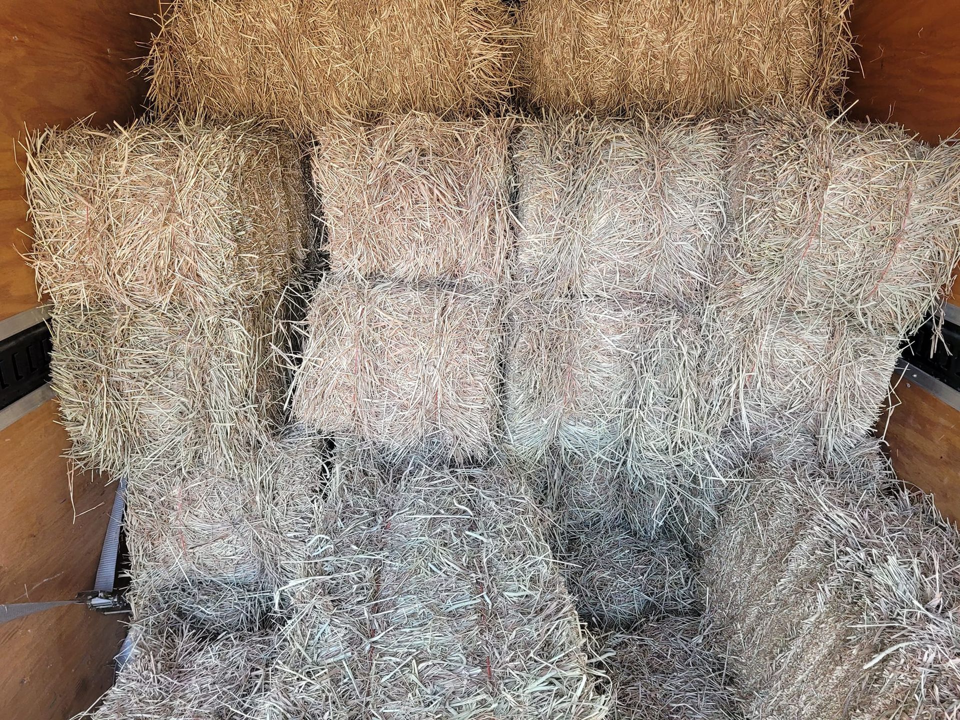A bunch of hay bales are stacked on top of each other in a trailer.