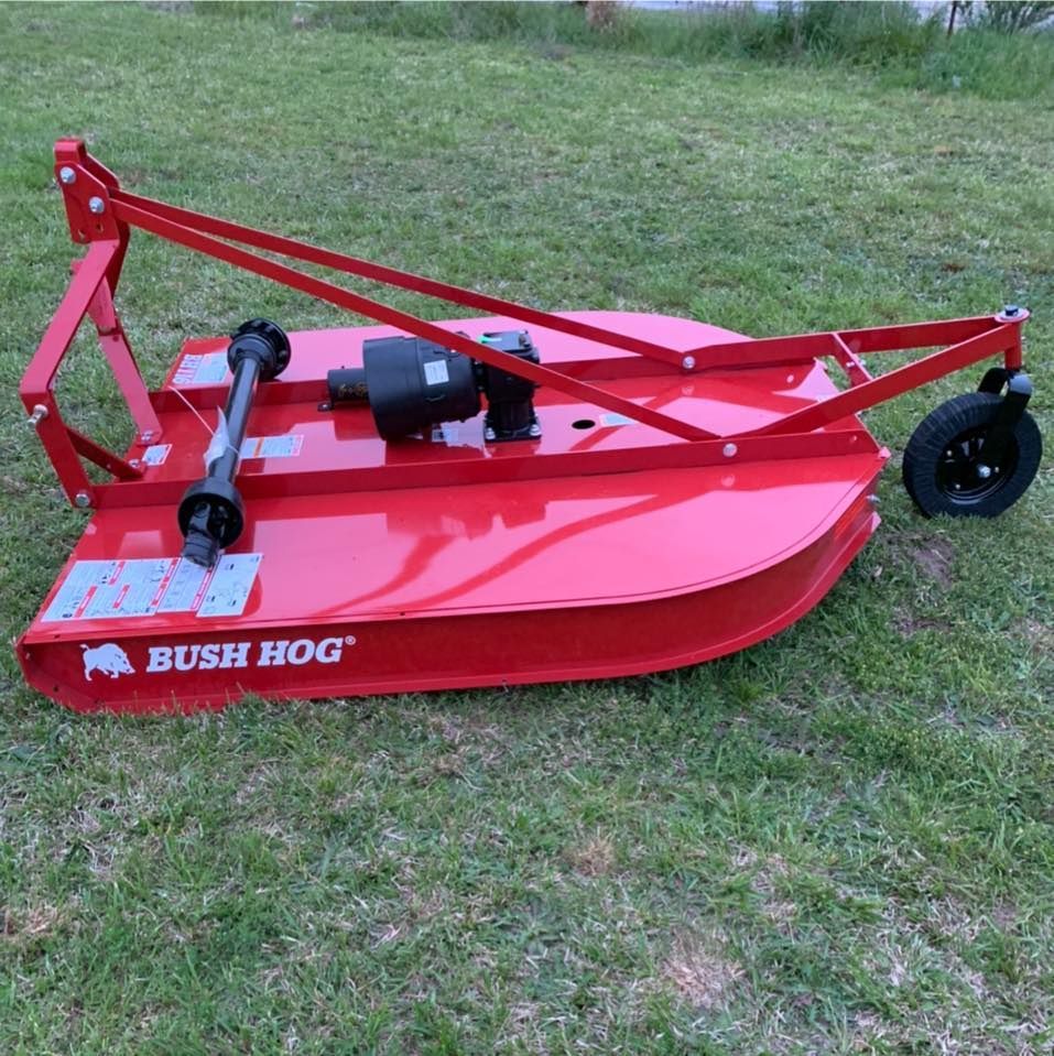 A red bush hog lawn mower is sitting in the grass
