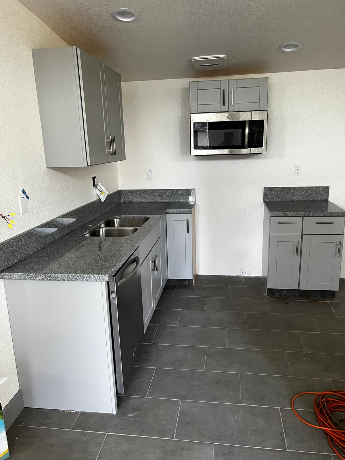 A kitchen with gray cabinets , granite counter tops , stainless steel appliances and a microwave.