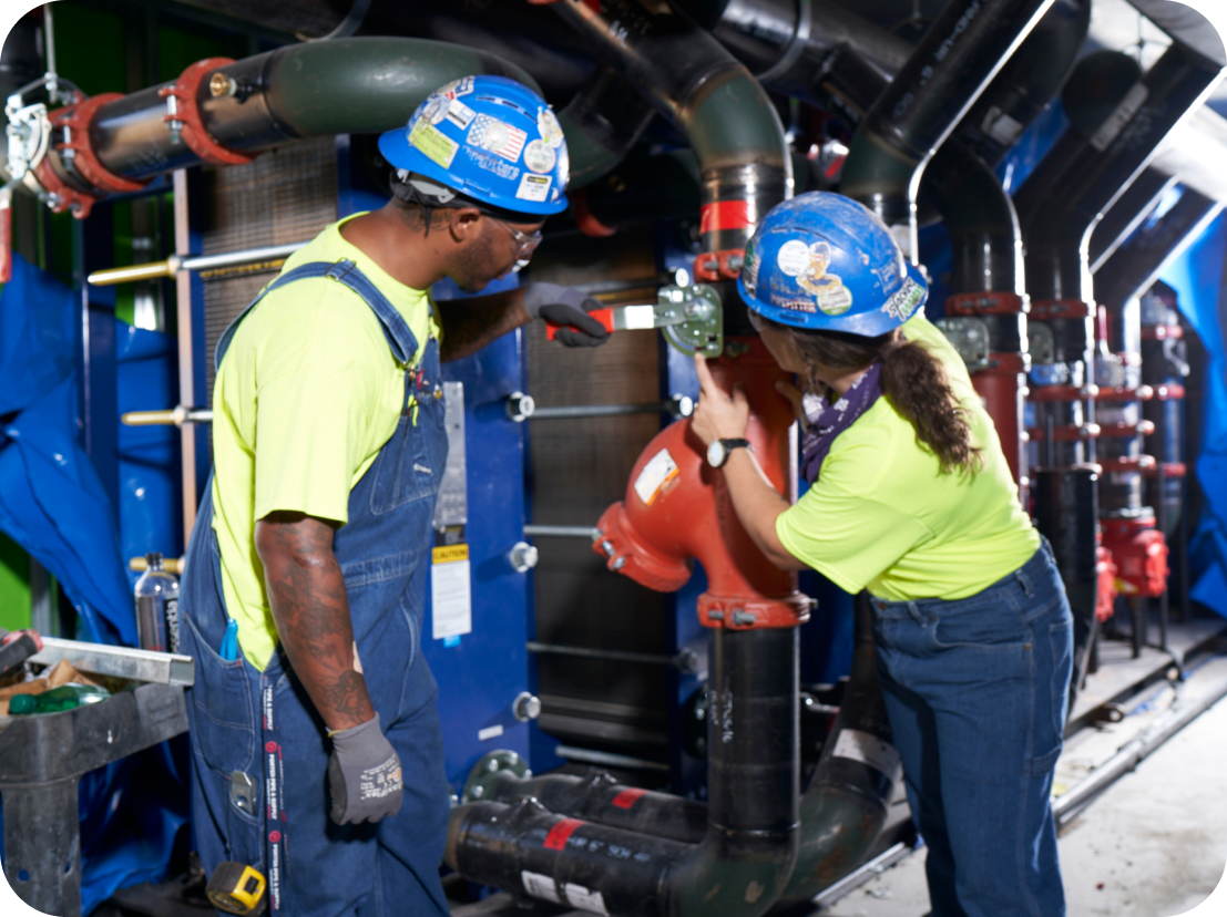 A man and a woman wearing hard hats are working on a machine