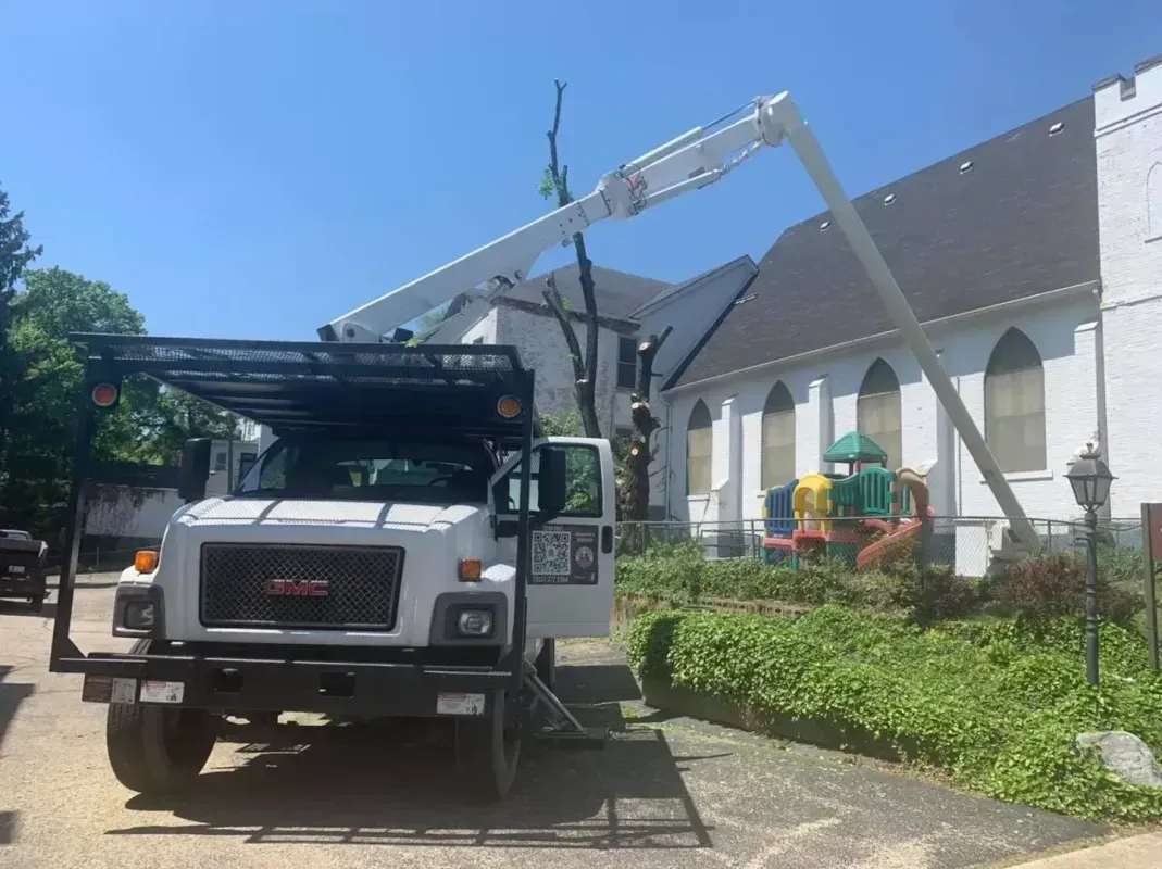 A white GMC utility bucket truck parked on gravel next to a white brick building with arched windows.