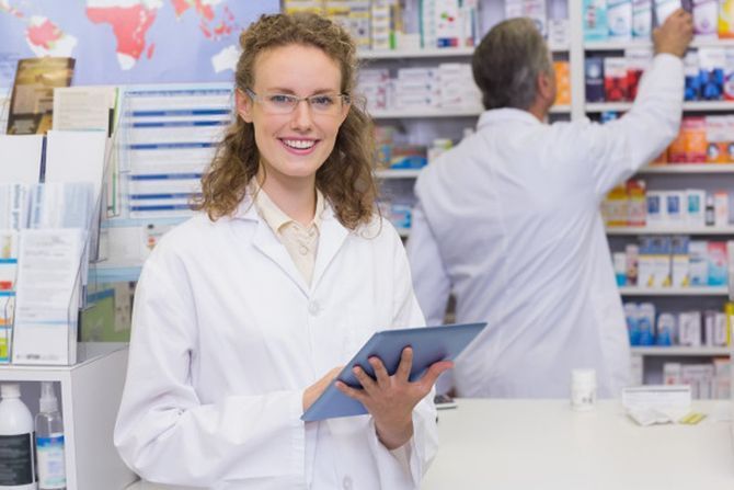A female pharmacist is holding a tablet in a pharmacy.