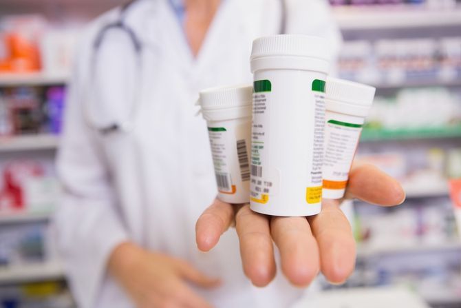 A female pharmacist is holding three bottles of pills in her hand.