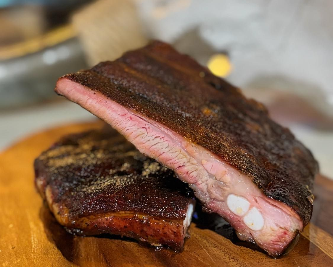 Smoked pork ribs on a wooden cutting board, with pink smoke ring and dark bark.