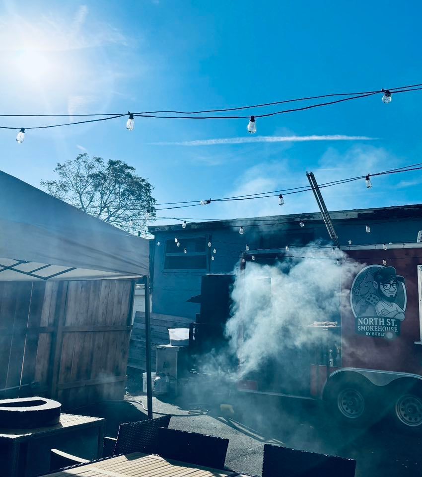 Smoky barbecue food truck, 56th St., with string lights and blue sky.