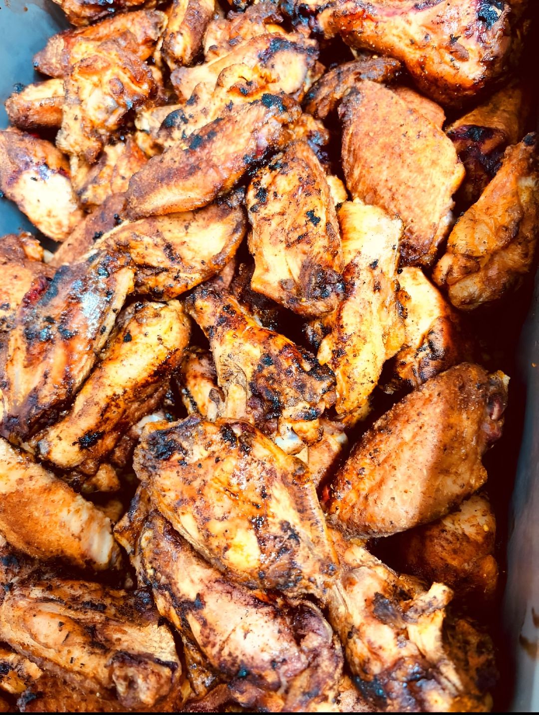 Pile of grilled chicken wings, seasoned with spices.