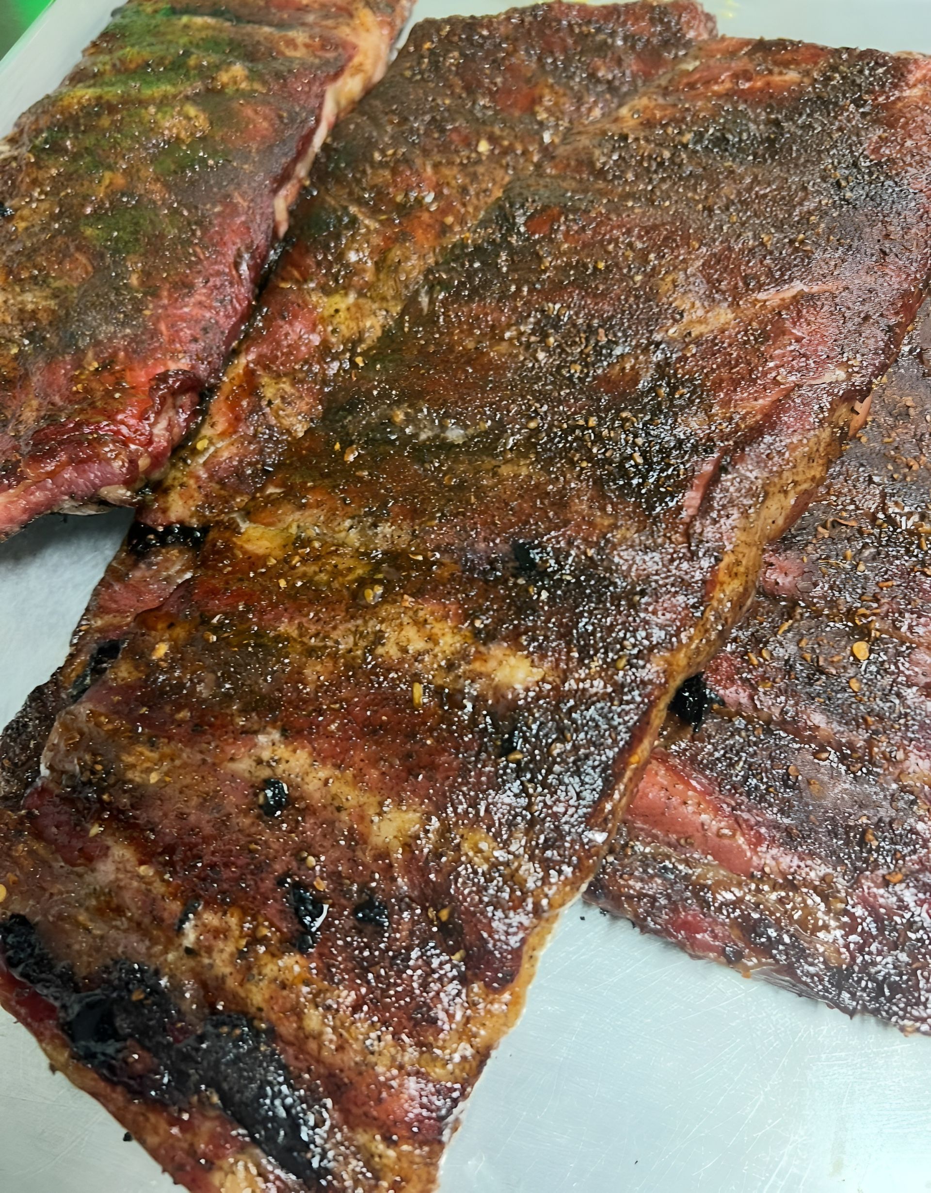 Smoked pork ribs seasoned with dry rub, arranged on a tray. Dark brown exterior, red meat visible.