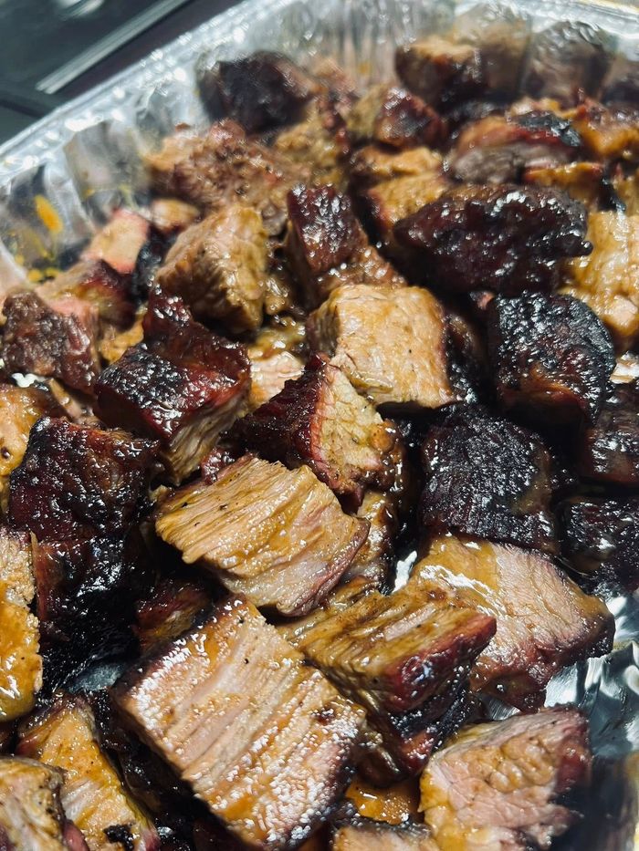 Close-up of a tray filled with smoked, glistening burnt ends of meat, various shades of brown and black.