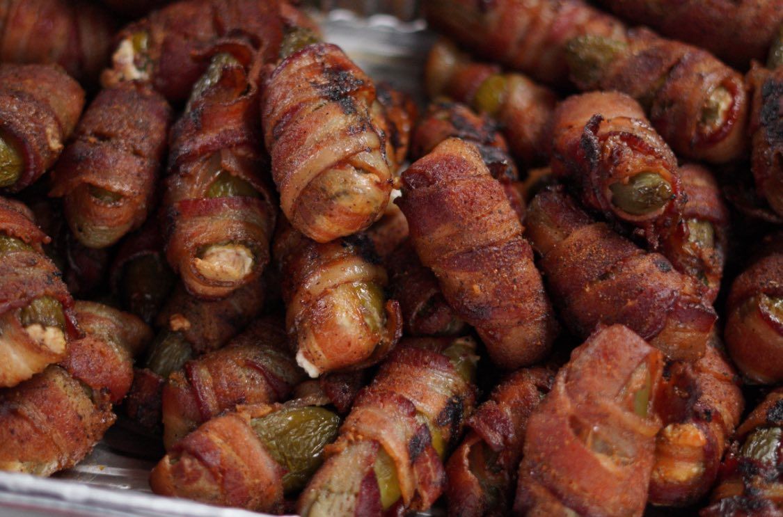 Bacon-wrapped jalapeño poppers, close up in a metal container, with a crispy, brown exterior and green peppers visible.