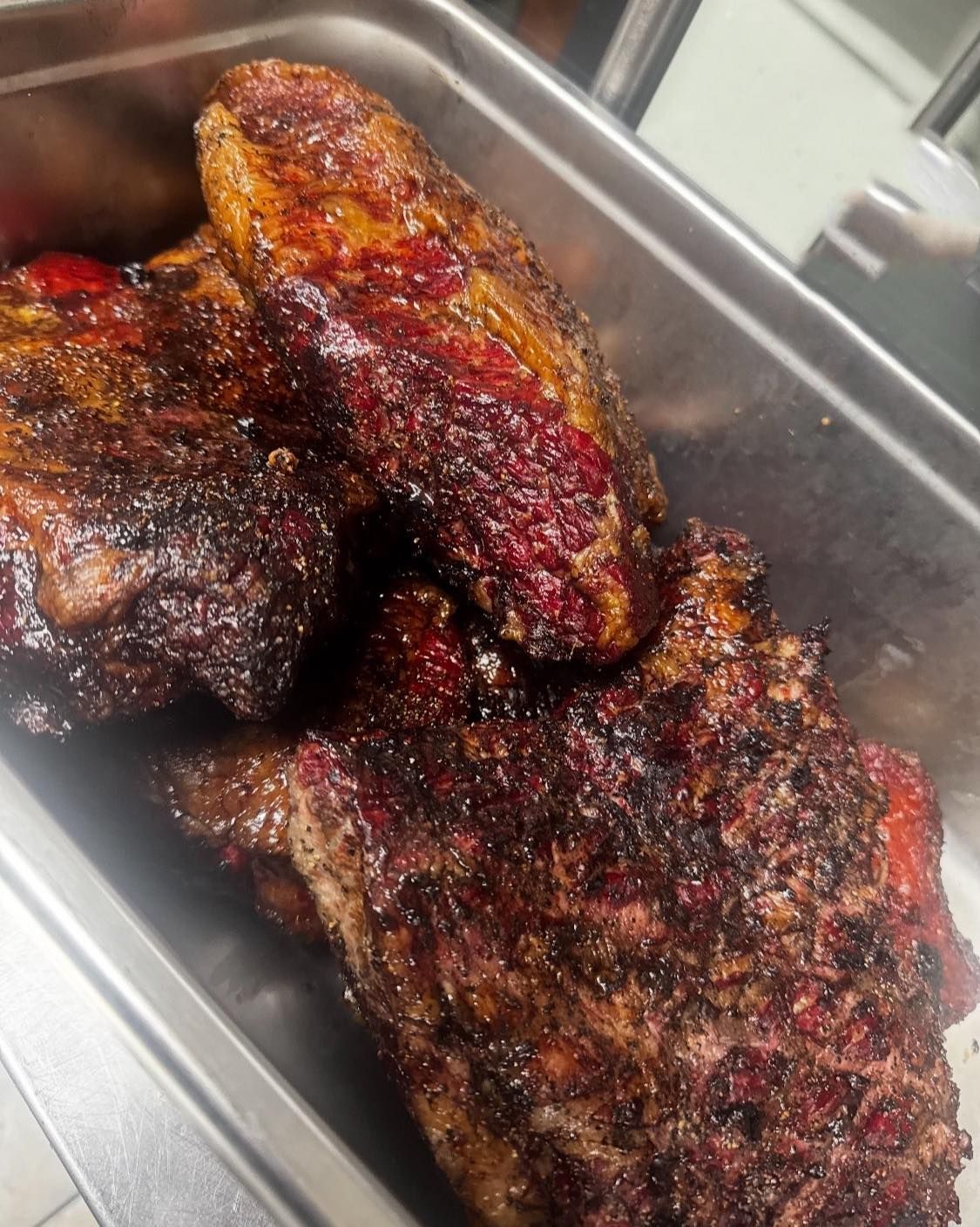 Smoked brisket in a metal tray; dark, charred exterior with a red meat interior.