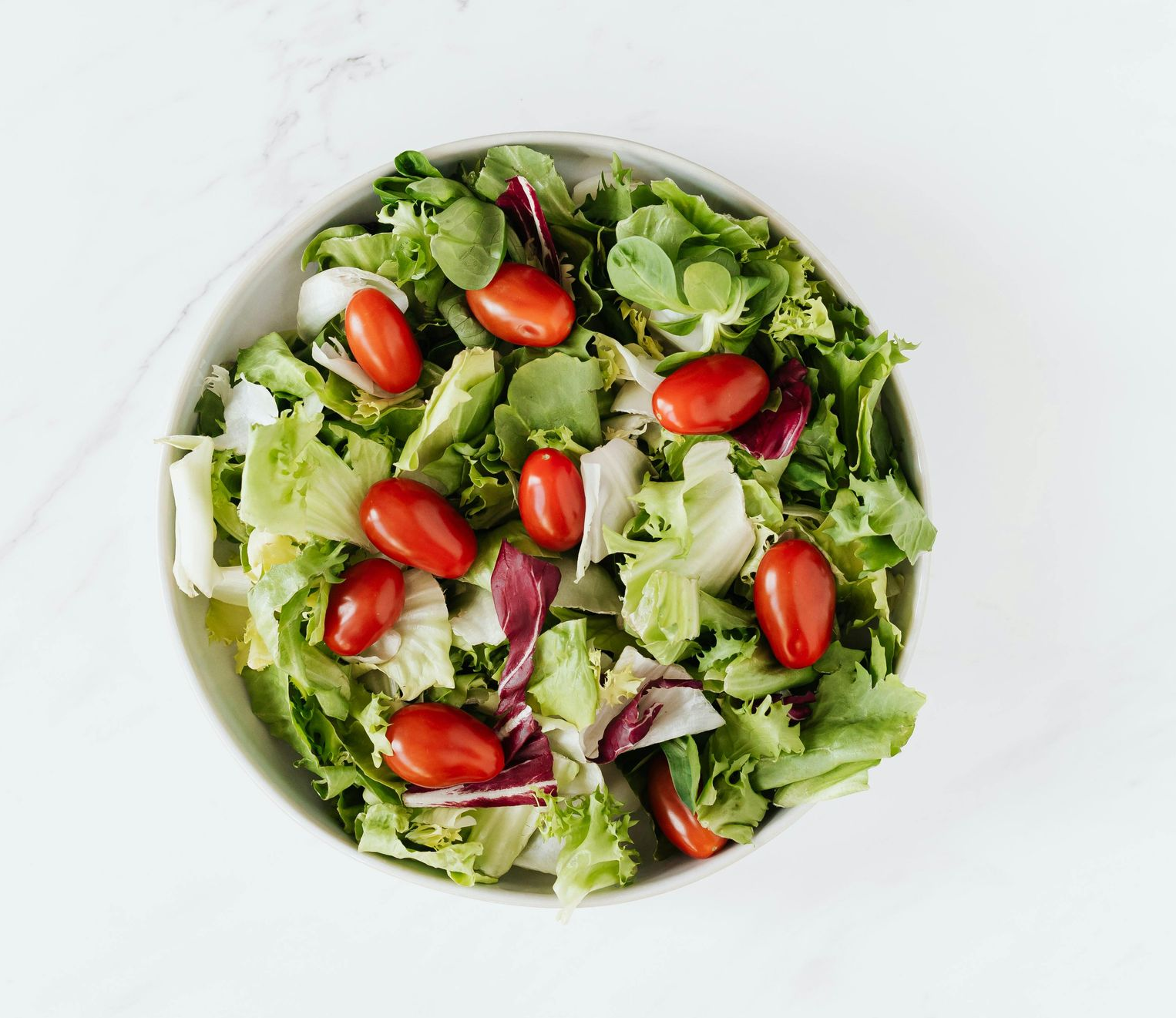 Salad bowl filled with lettuce and cherry tomatoes on a white surface.
