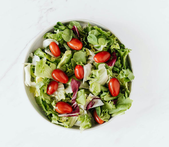 Salad bowl filled with lettuce and cherry tomatoes on a white surface.